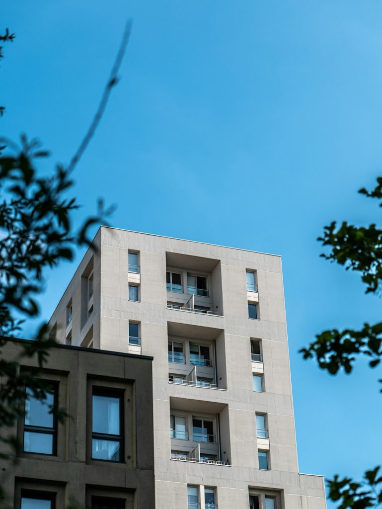 A modern building in the city of Nantes, captured in a low-angle shot. Reflections of the sky and clouds on the building can be seen. Blue and cloudy sky in the background. Sunny.